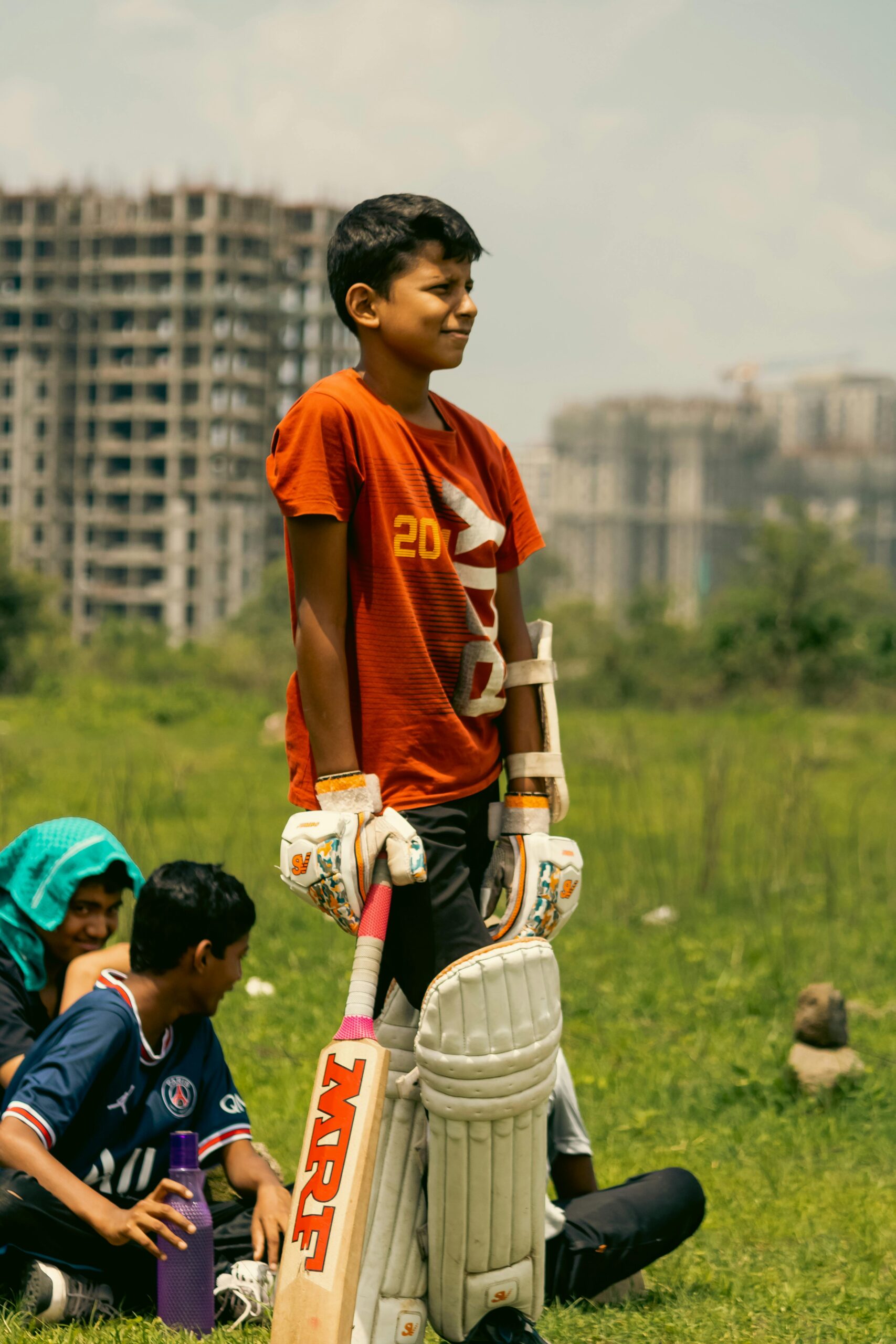 Children enjoying a cricket game outdoors near city buildings.