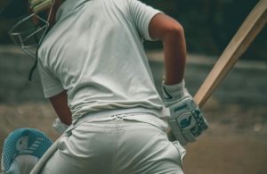 pexels-photo-12732864-12732864 A young male cricketer wearing full gear, ready to bat on an outdoor field.